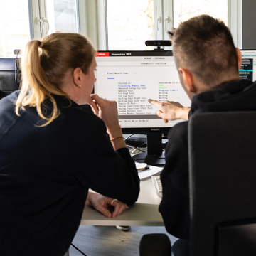 Teaserbild zeigt eine Frau und einen Mann vn hinten am Schreibtisch vor einem Monitor.