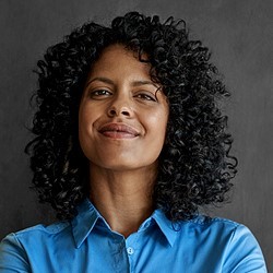 Auf dem Bild ist das Portrait einer Frau vor einem grauen Hintergrund zu sehen.