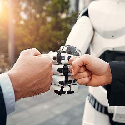 Drei Fäuste werden zusammengestoßen. Zwei sind menschliche Fäuste, eine ist eine Roboterfaust.