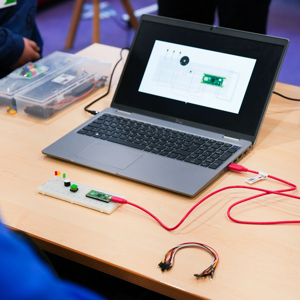 Ein Laptop steht auf einem Tisch, daran per USB-Kabel angeschlossen eine selbst gebaute Ampelschaltung mit LEDs ind Rot, Gelb und Grün.