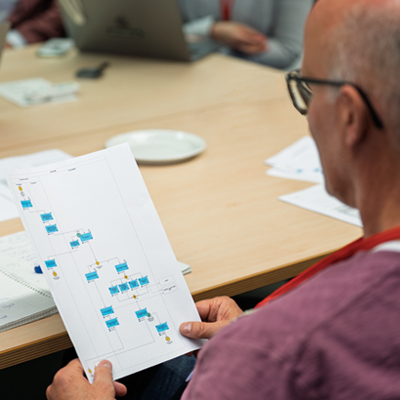 Ein Mann sitzt an einem Tisch und hält in den Händen ein Blatt Papier mit einem Prozessdiagramm.